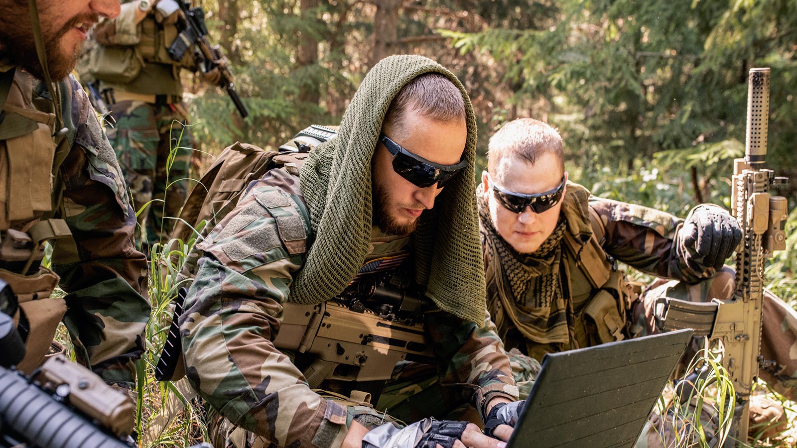 Men in camouflage gear working on a laptop in the field
