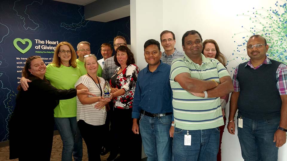 A group of employees in front of a Heart of Giving wall and holding an award