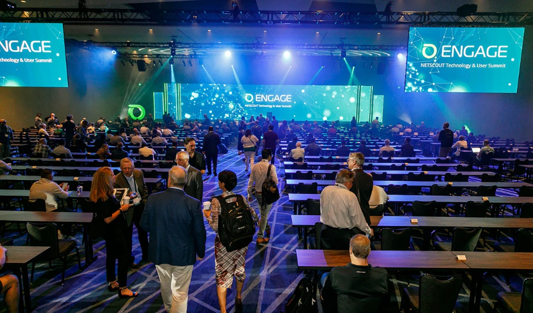 People in business suits mingling before ENGAGE keynote in large partially-filled ballroom