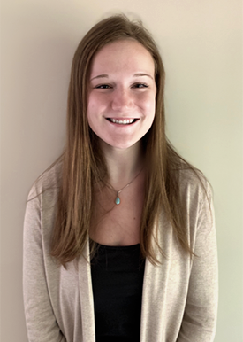 Erin Hill, a young woman with long brown hair wearing a beige sweater and black shirt