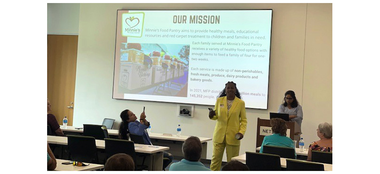 Woman in yellow pantsuit presenting an Our Mission slide for Minnie's Food Pantry