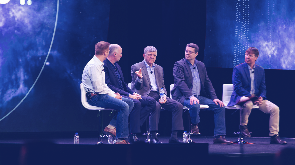 NETSCOUT COO Michael Szabados sits on a panel with with four other men on stage at an event.