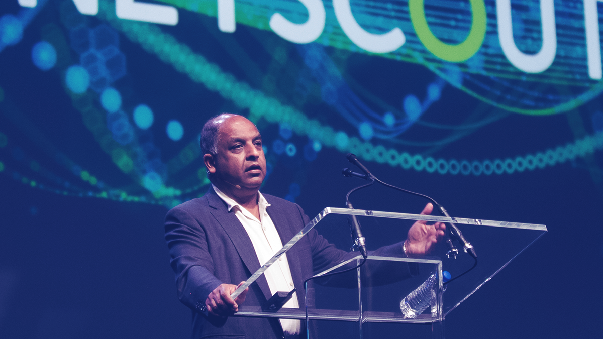 NETSCOUT CEO Anil Singhal, presenting at a podium in front of a large screen with the NETSCOUT logo.