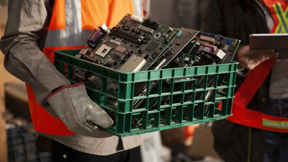Worker carrying green plastic basket of old CPU parts