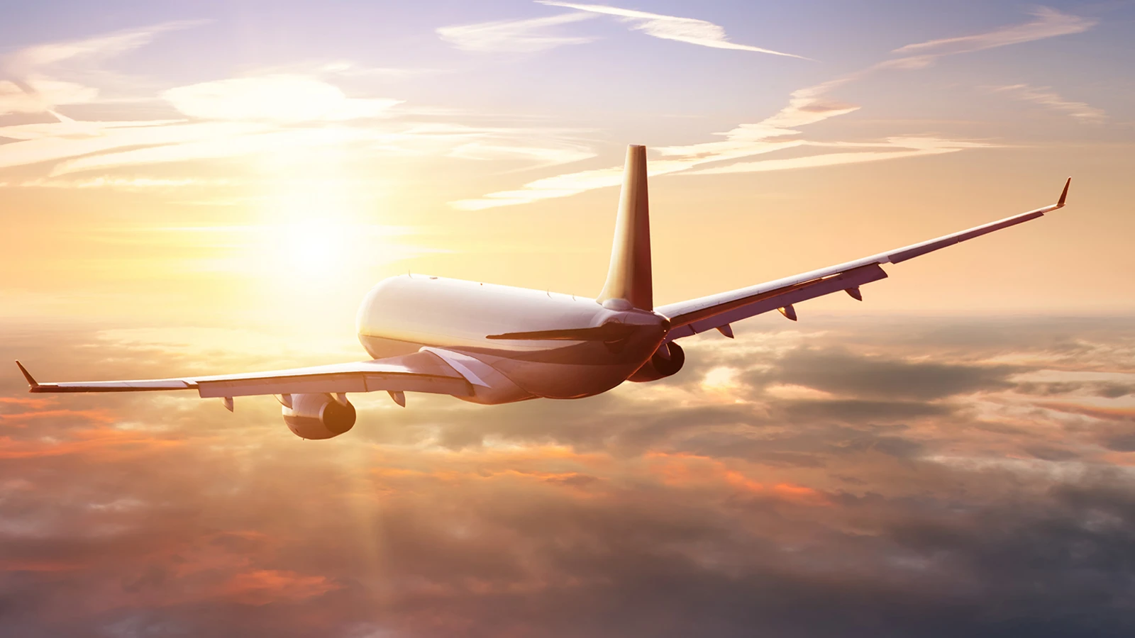Passenger airplane soaring into the sunset above the clouds 