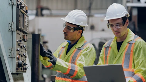 Two men with hardhats on equipment and laptop