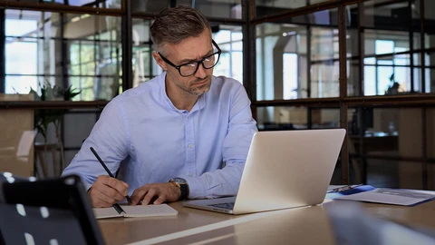 Man reviewing laptop at desk taking notes