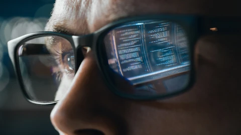 Close up shot of a person and monitor image is reflecting in their glasses