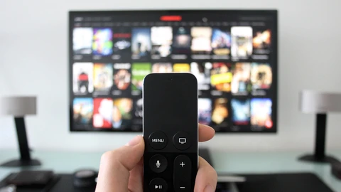 Close up picture of hand holding a TV Remote with blurred TV displaying different show options in background