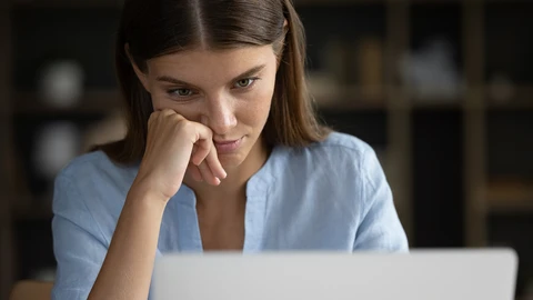 Woman sitting in front of laptop looking at screen with hand fold on her cheek