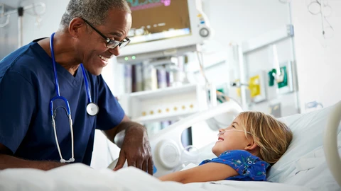 Doctor smiling looking down at a happy child patient in a hospital bed