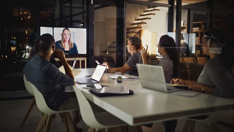 People sitting at conference room table watching video conference on main screen.