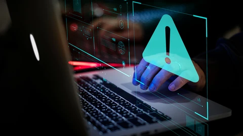 Hand on laptop with exclamation symbol.