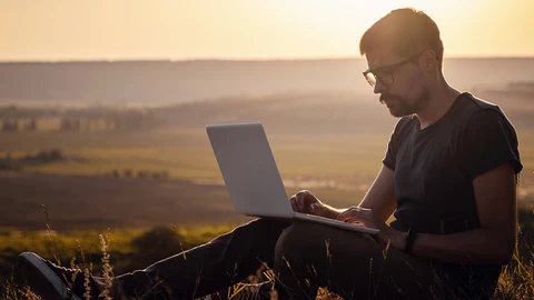 Person sitting in country field on laptop