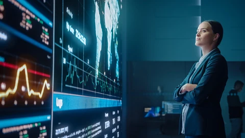 Woman with arms folded looking at reports on large wall monitor