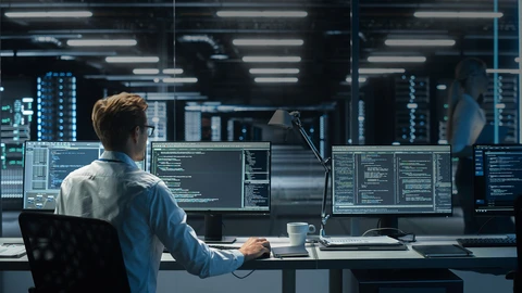Person sitting in front on 3 monitors overlooking datacenter