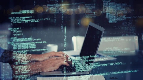 Hands on laptop keyboard with snipets of code in foreground.