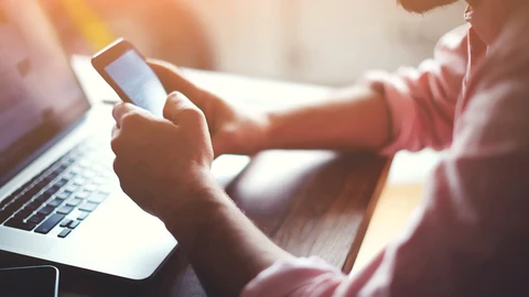 Woman holding mobile phone and working on laptop