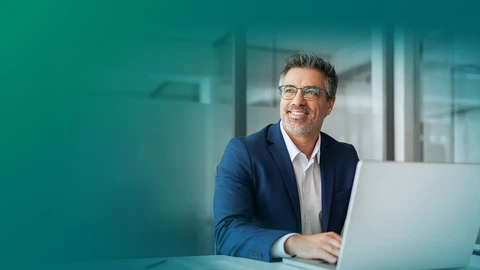 Business professional in a blue suit working on a laptop in a modern office with glass walls.
