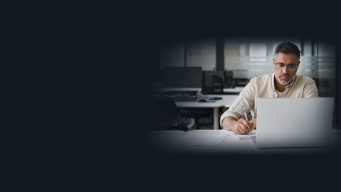 Man with laptop writing on a pad of paper