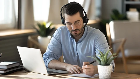 Man with laptop writing on a pad of paper