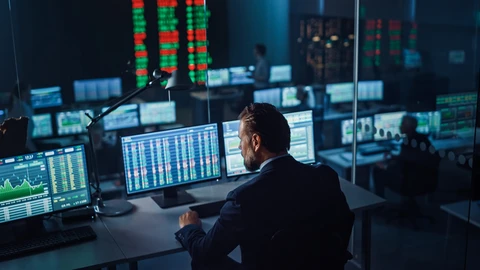 Worker on computer with many screens around showing dashboards