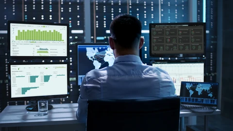 Man at NOC workstation review data on multiple monitors