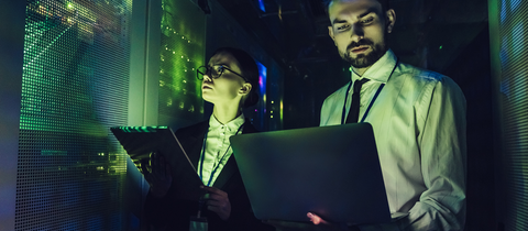 2 people on laptop in dark data center