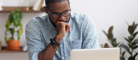 Man with hand on his chin in shape of a fist looking at laptop