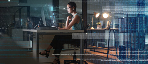 person sitting at desk at night in a glass conference room