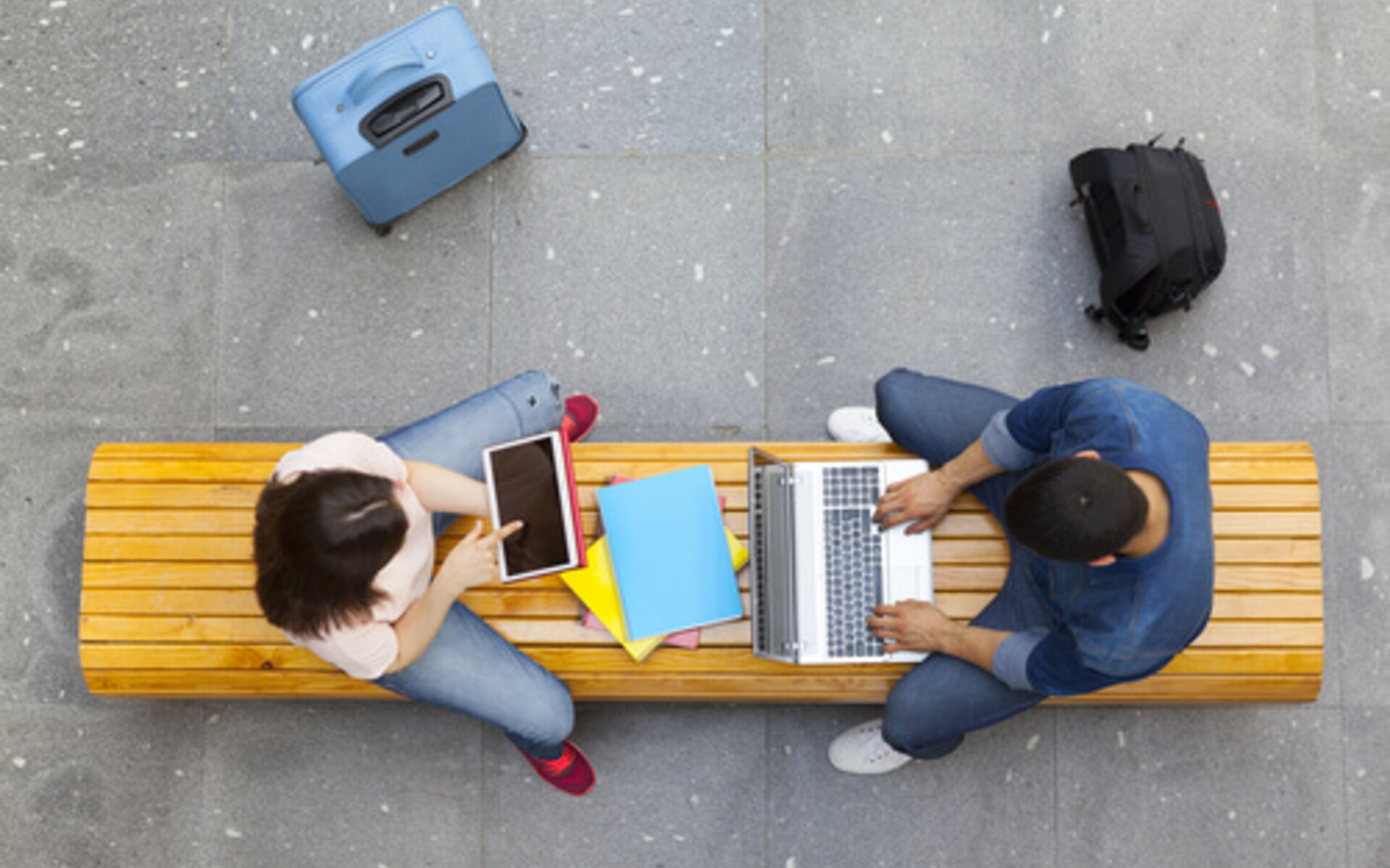 Students working on laptops seated on a bench