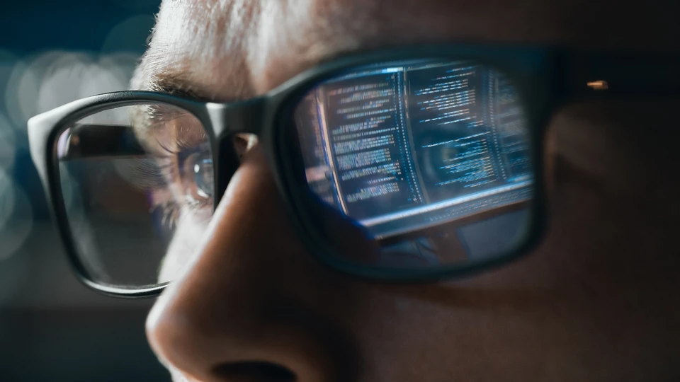Person working on computer with code reflected on glasses