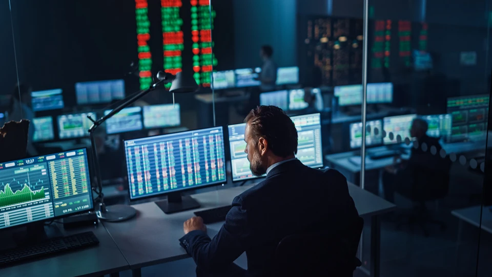 Worker on computer with many screens around showing dashboards
